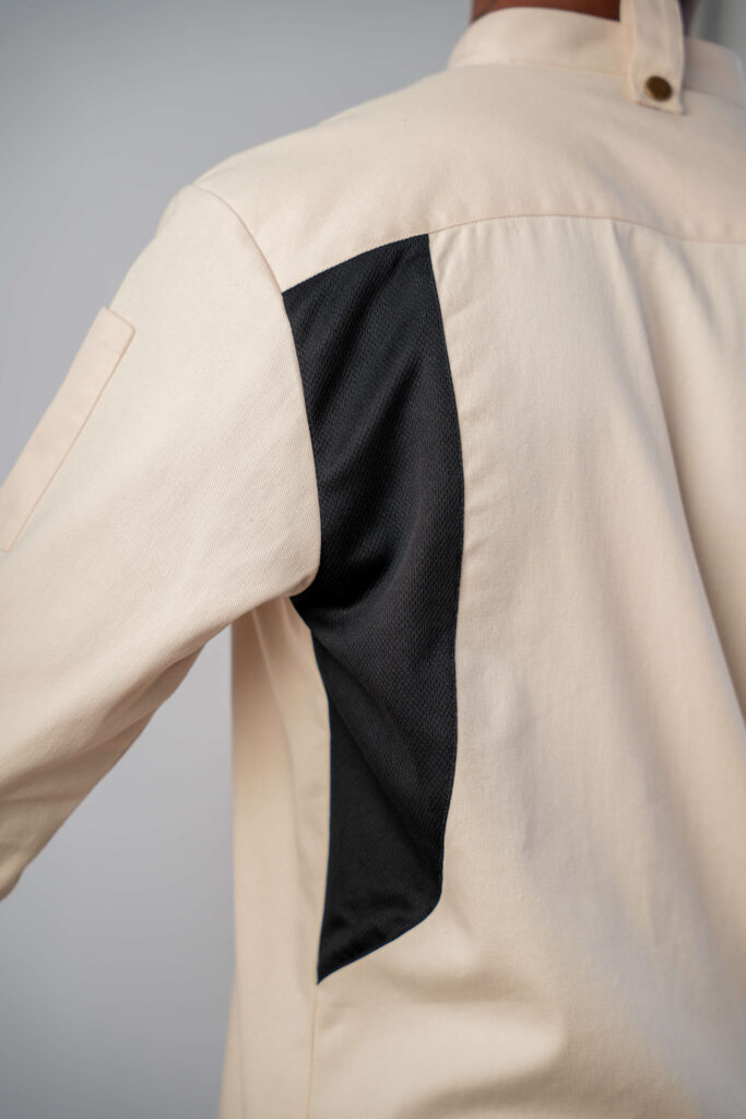 Model wearing a cream chef's jacket with black mesh ventilation panels along the sides and underarms